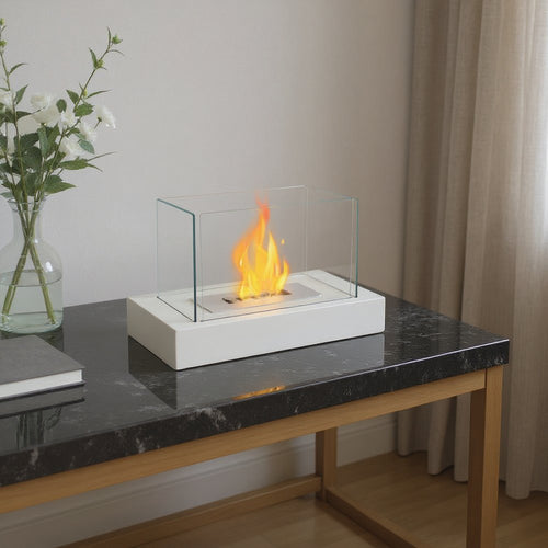 White and clear glass tabletop bioethanol fireplace with visible flames on a dark marble table with a vase of white flowers.