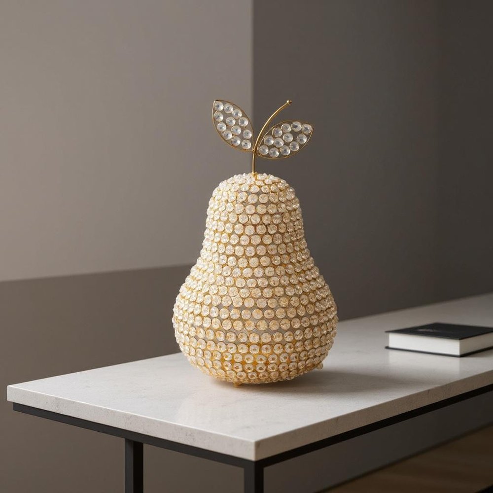 18" Gold Aluminum And Faux Crystal Decorative Pear styled in a furnished interior with a dark wall on a dark wood floor.