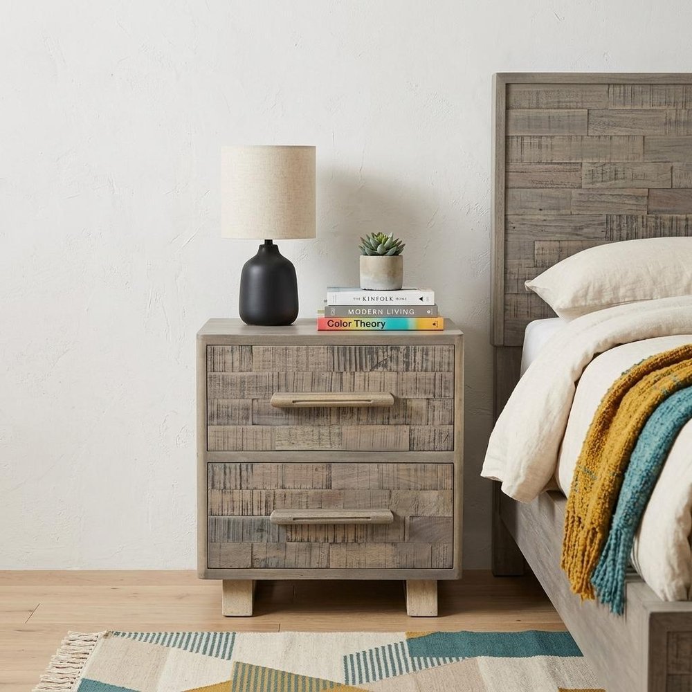 26" Gray Solid Wood Carved Geometric Two Drawer Nightstand styled in a furnished interior with an off-white wall on a wood floor.