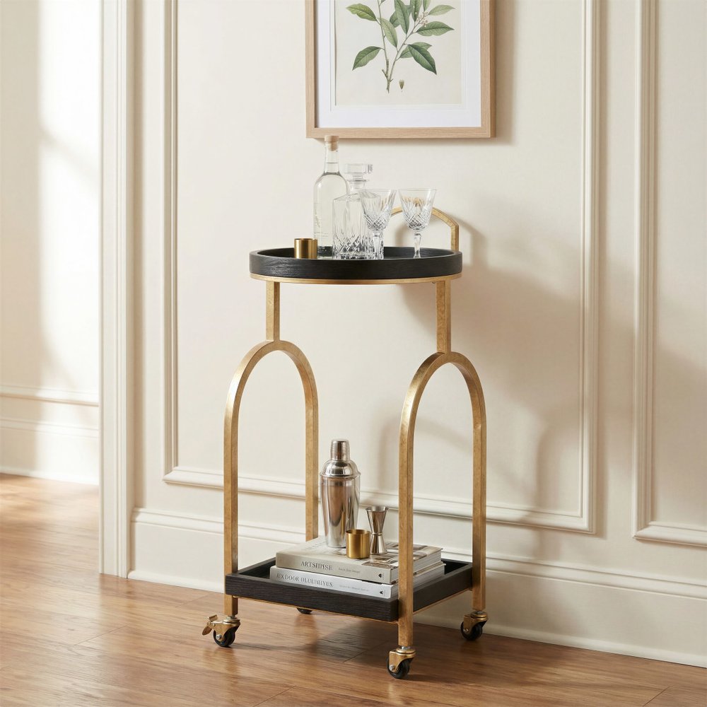 17" Black And Brass Steel and Solid Wood Distressed Round Rolling Bar Cart styled in a furnished interior with an off-white wall on a wood floor.
