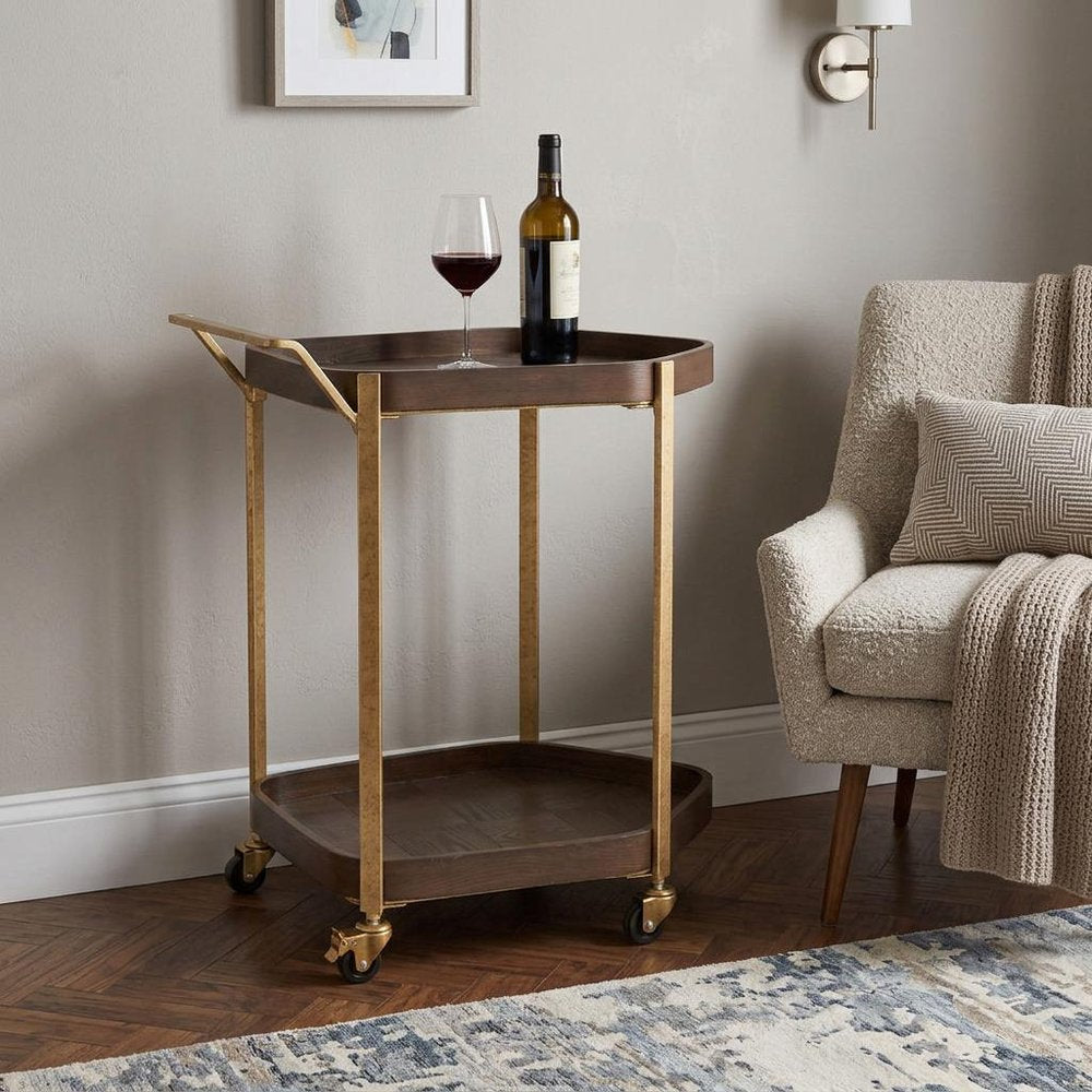 27" Walnut And Brass Wood and Steel Rolling Bar Cart styled in a furnished interior with a light gray wall on a dark wood floor.