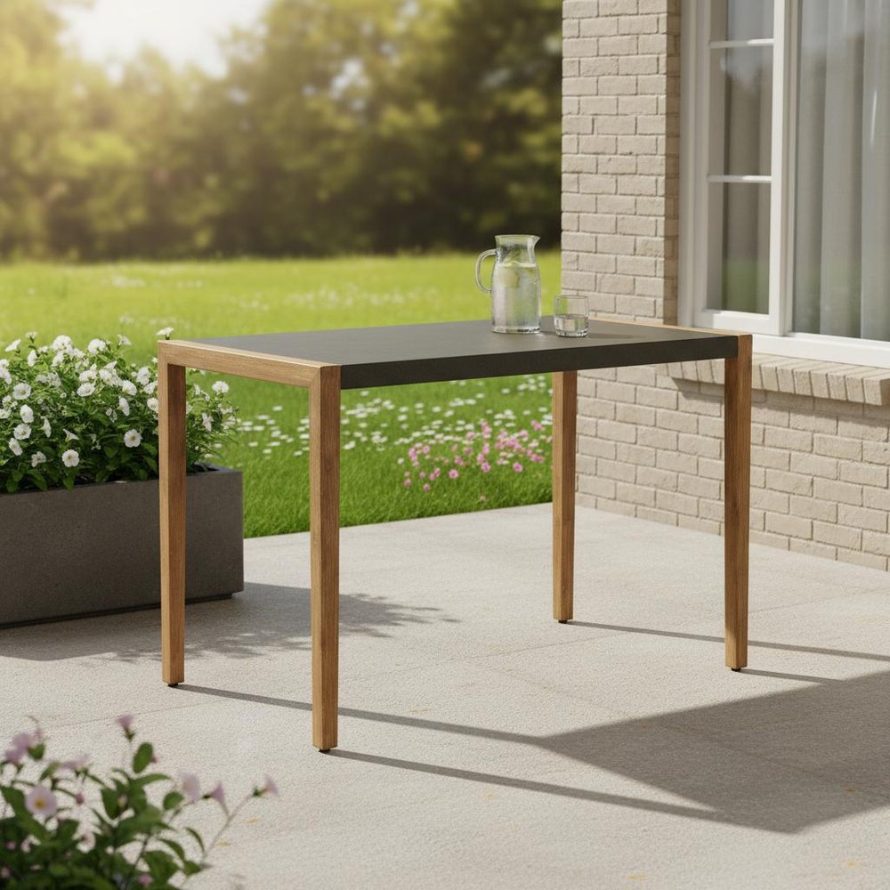 56" Gray And Natural Faux Concrete And Solid Wood Outdoor Bar Table shown outdoors on a tiled patio with greenery in tan wood.