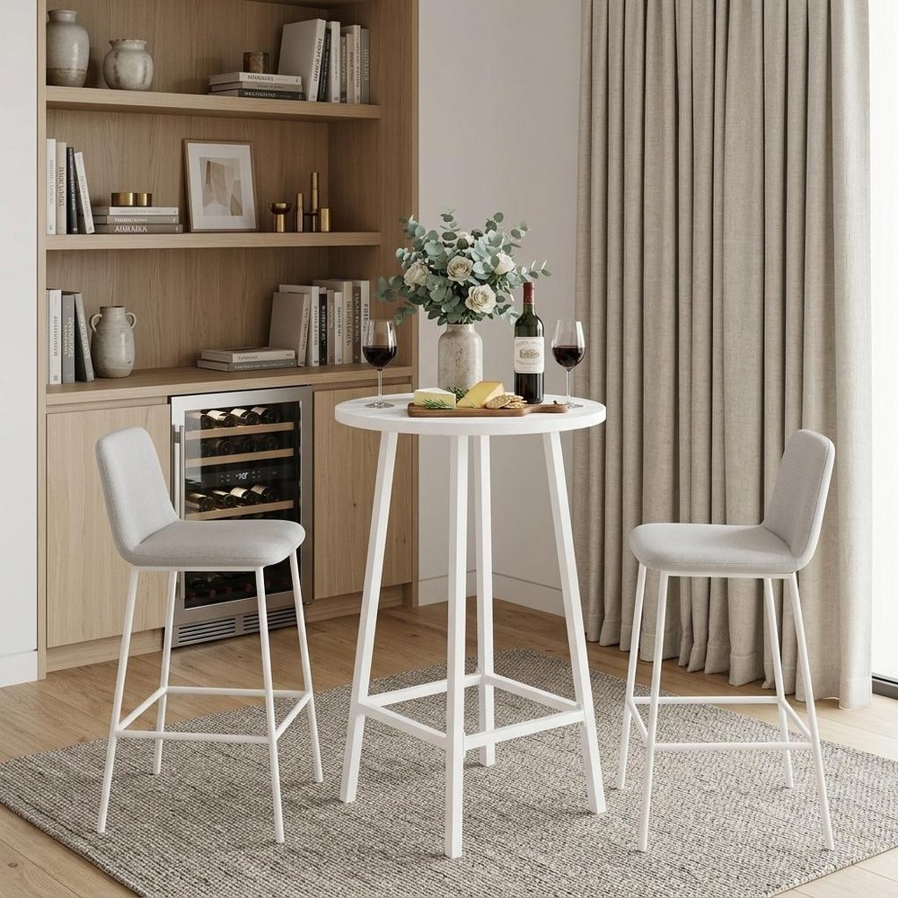 24" White Aluminum Slat Rounded Outdoor Bar Table styled in a furnished interior with a tan wall on a wood floor.