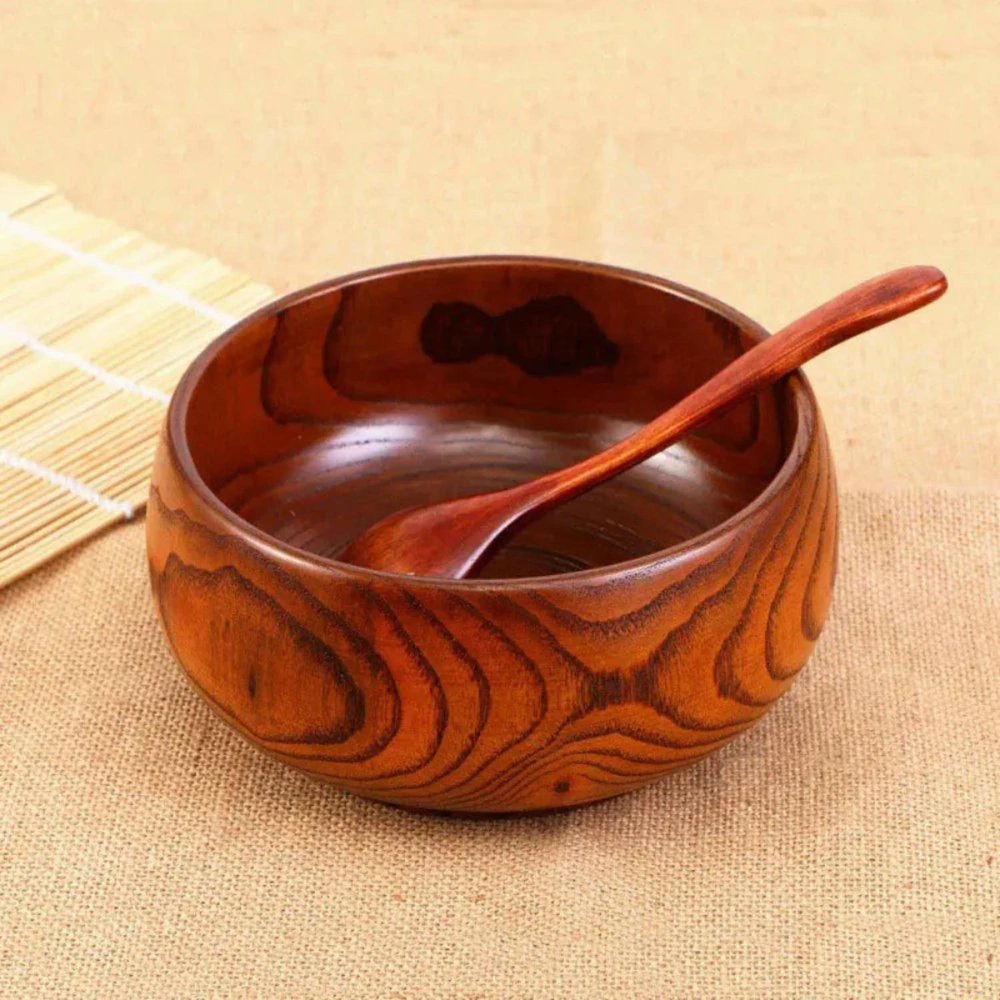 A brown solid wood round serving bowl with a wooden spoon rests on a burlap background with a bamboo mat.