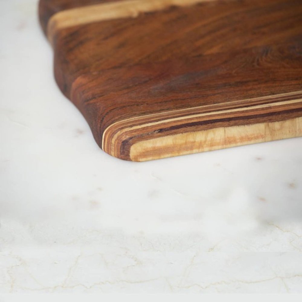 17" Brown Solid Wood Cutting Board styled in a furnished interior with a dark brown wall on a off-white floor.
