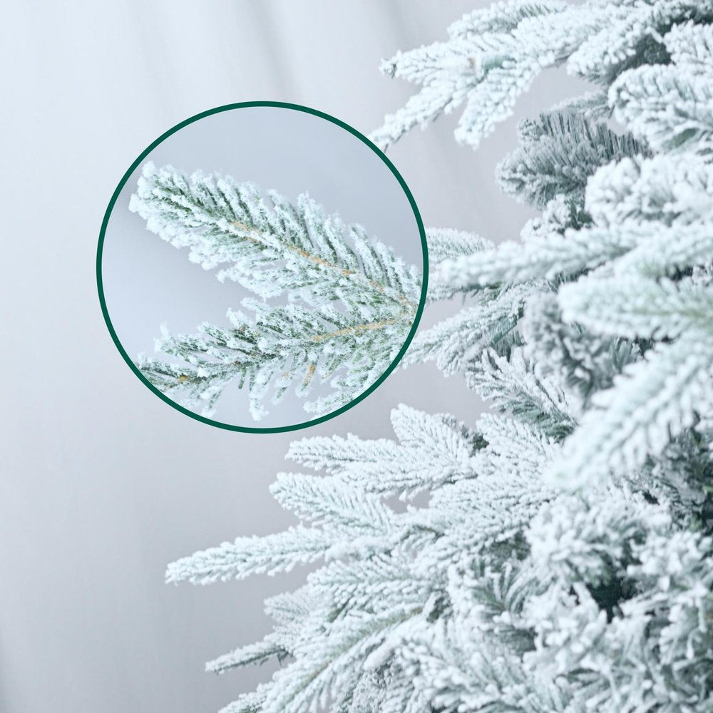 Close-up of a flocked pine Christmas tree branch with a frosted appearance against a light gray background.