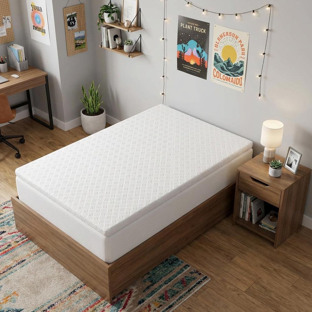 4" White Memory Foam Twin Mattress Topper styled in a furnished interior with a light gray wall on a dark wood floor.