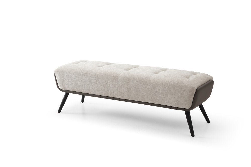 A tufted beige upholstered bench with dark gray faux leather accents and black steel legs on a white background.
