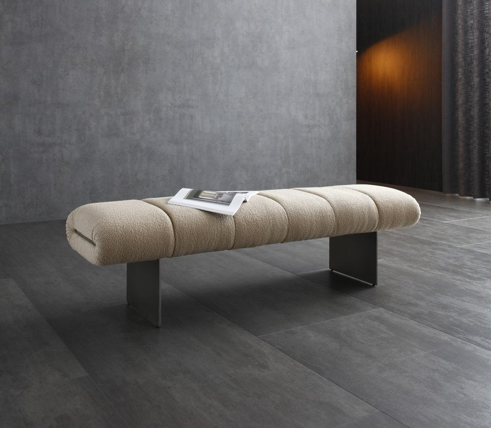 Beige boucle upholstered bench with steel legs on a dark tiled floor in a modern room.