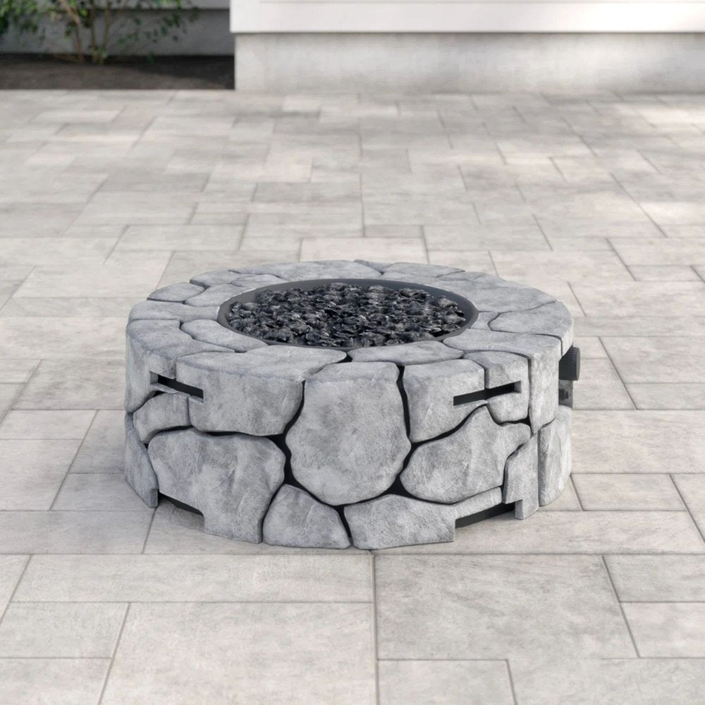 Round gray concrete fire pit with black lava rocks on a light gray paved patio.
