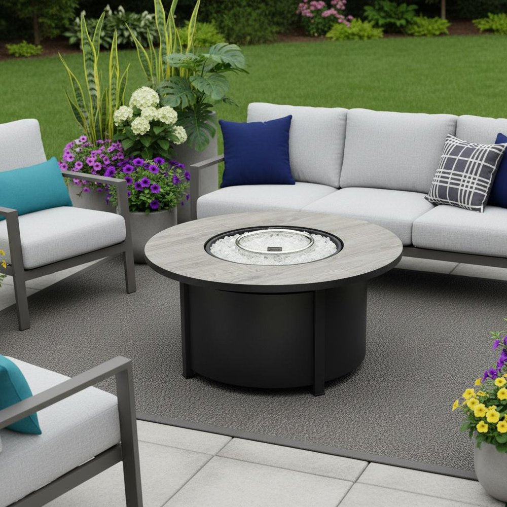 50000 BTU 30" Black Steel Propane Column Fire Pit With Cover shown outdoors on a tiled patio with greenery.