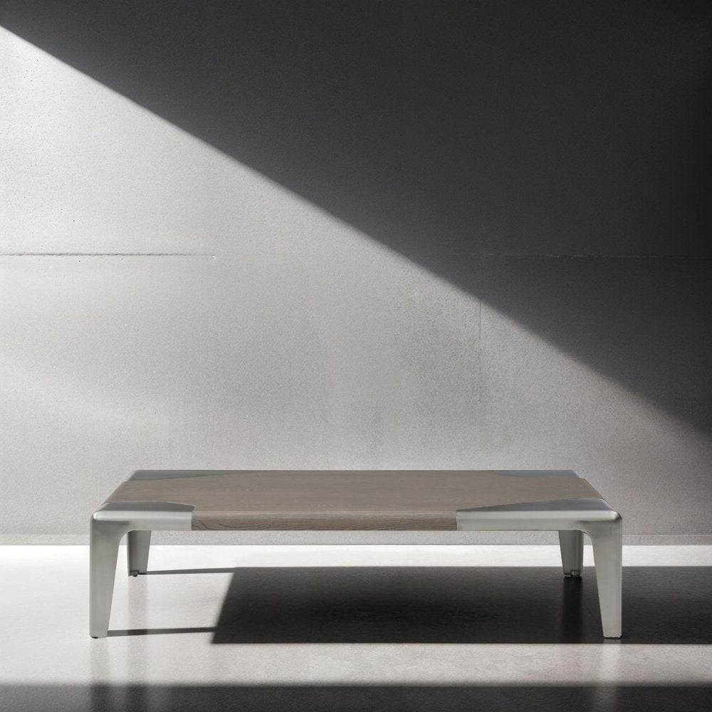 Rectangular coffee table with light gray wood top and silver stainless steel frame against a gray wall with diagonal light and shadow.