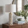 27" White Novelty Table Lamp With Drum Shade displayed on a dark wood tabletop in a furnished interior against a light gray wall.