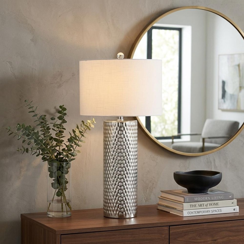 30" Silver Table Lamp With Drum Shade displayed on a dark wood tabletop in a furnished interior against a tan wall.
