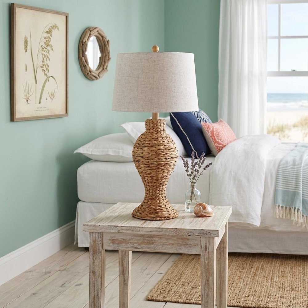31" Natural Water Hyacinth Urn Table Lamp With Drum Shade shown outdoors on an outdoor setting with greenery in tan.