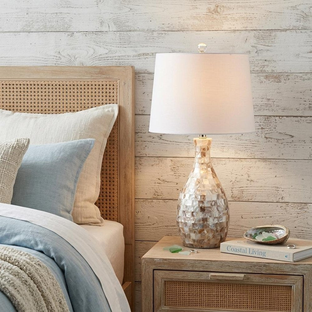 27" Ivory And Beige Novelty Table Lamp With Drum Shade displayed on a dark wood tabletop in a furnished interior against a cream wall.