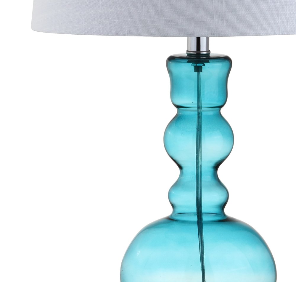 Close-up of a blue glass table lamp with a white drum shade against a white background.