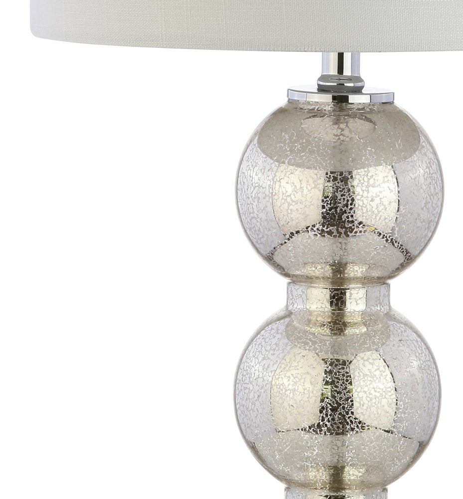 Close-up of a silver mercury glass table lamp with a white drum shade against a white background.