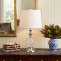 24" Silver Novelty Table Lamp With Drum Shade displayed on a tabletop in a furnished interior against a cream wall.