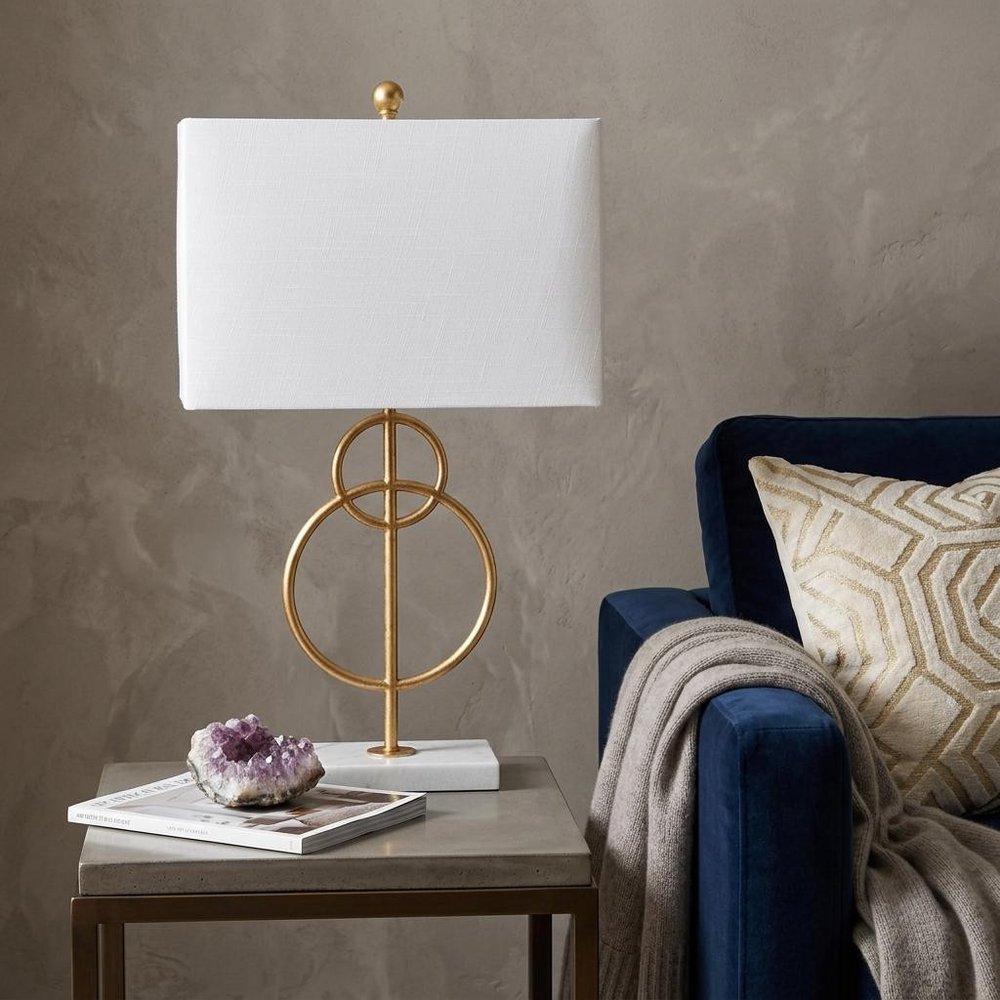 26" White Novelty Table Lamp With Shade displayed on a dark wood tabletop in a furnished interior against a tan wall.