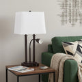 24" Antiqued Bronze Swing Arm Novelty Table Lamp With Shade displayed on a dark wood tabletop in a furnished interior against a light gray wall.