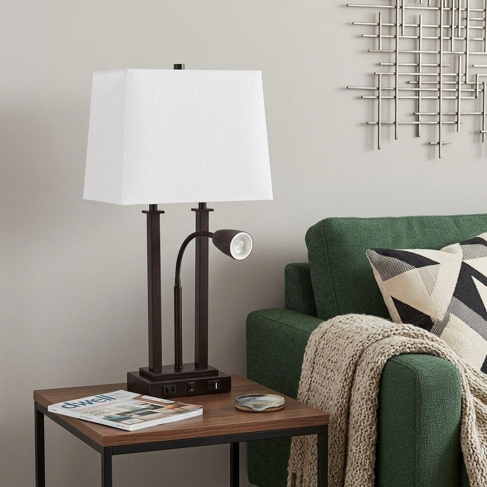 24" Antiqued Bronze Swing Arm Novelty Table Lamp With Shade displayed on a dark wood tabletop in a furnished interior against a light gray wall.