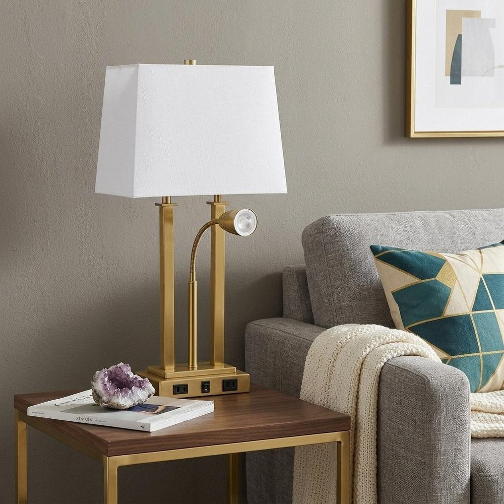 24" Gold Swing Arm Novelty Table Lamp With Shade displayed on a dark wood tabletop in a furnished interior against a light gray wall.