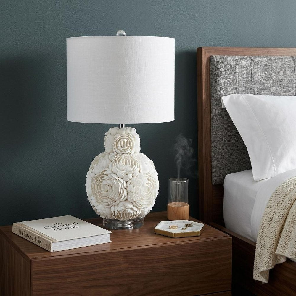 24" Off White Seashell Table Lamp With White Drum Shade shown outdoors on an outdoor setting in off-white.