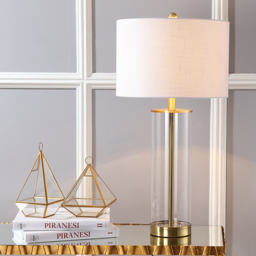 29" Gold Table Lamp With Drum Shade displayed on a wood tabletop in a furnished interior against a light gray wall.