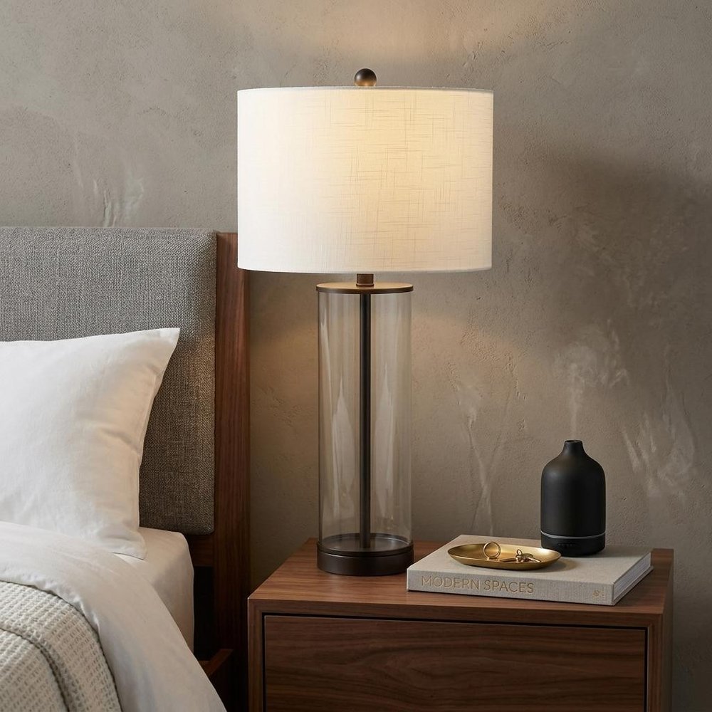 29" Antiqued Bronze Table Lamp With Drum Shade displayed on a dark wood tabletop in a furnished interior against a tan wall.
