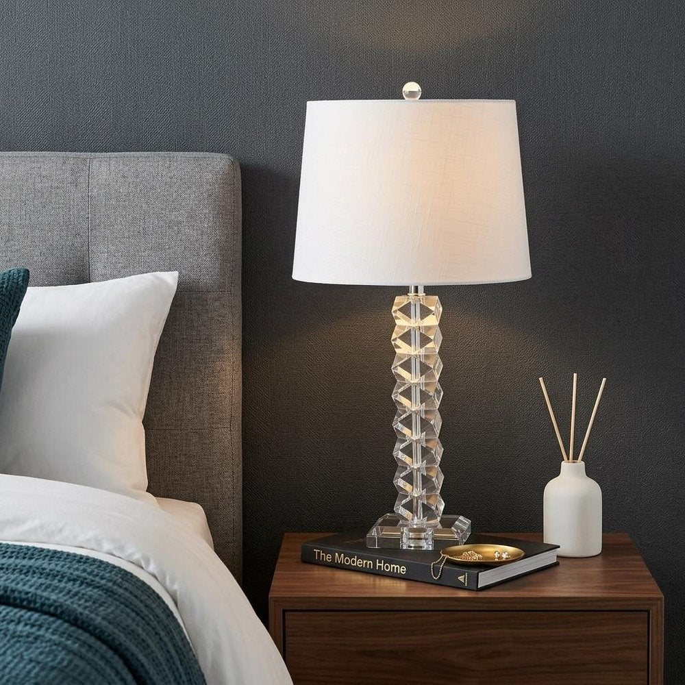 26" Clear Novelty Table Lamp With Drum Shade displayed on a dark wood tabletop in a furnished interior against a dark wall.