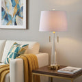 30" Gold Novelty Table Lamp With Empire Shade displayed on a dark wood tabletop in a furnished interior against a light gray wall.