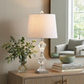 26" Silver Urn Table Lamp With Empire Shade displayed on a wood tabletop in a furnished interior against a tan wall.