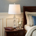 27" Silver Novelty Bedside Lamp With Drum Shade styled in a furnished interior with a gray wall on a black floor.