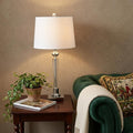 28" Silver Table Lamp With Drum Shade displayed on a tabletop in a furnished interior against a tan wall.
