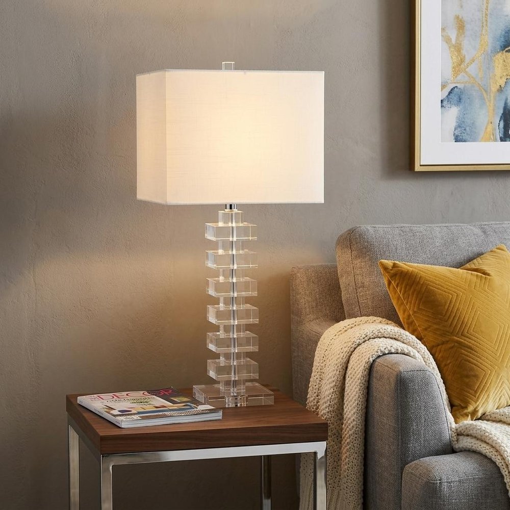 28" Clear Novelty Table Lamp With Shade displayed on a dark wood tabletop in a furnished interior against a tan wall.
