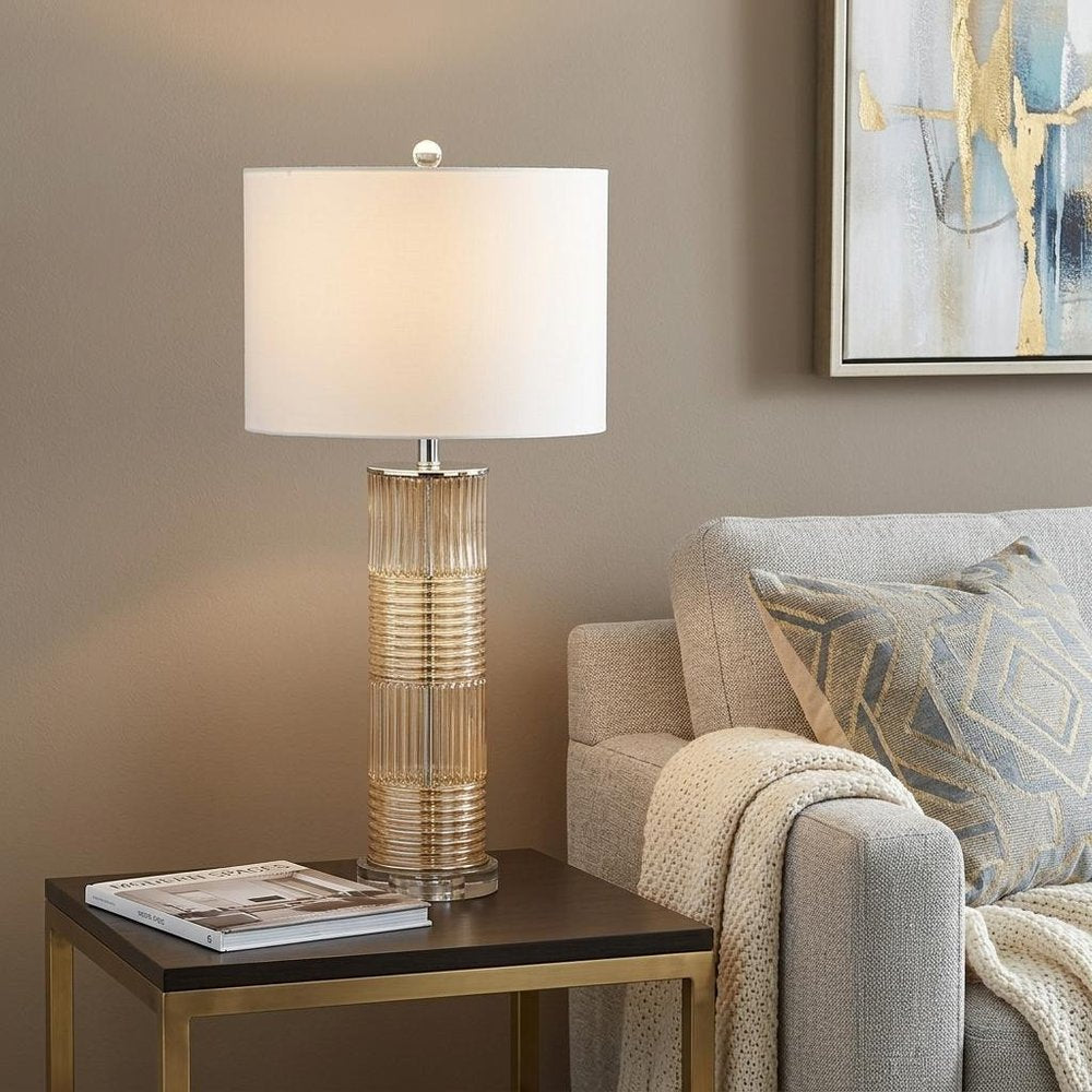 30" Clear Table Lamp With Drum Shade displayed on a dark wood tabletop in a furnished interior against a tan wall.