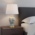 24" Gold And Off White Urn Table Lamp With Empire Shade displayed on a tabletop in a furnished interior against a light gray wall in off-white.