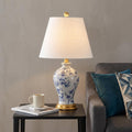 24" Gold Urn Table Lamp With Empire Shade displayed on a tabletop in a furnished interior against a tan wall.