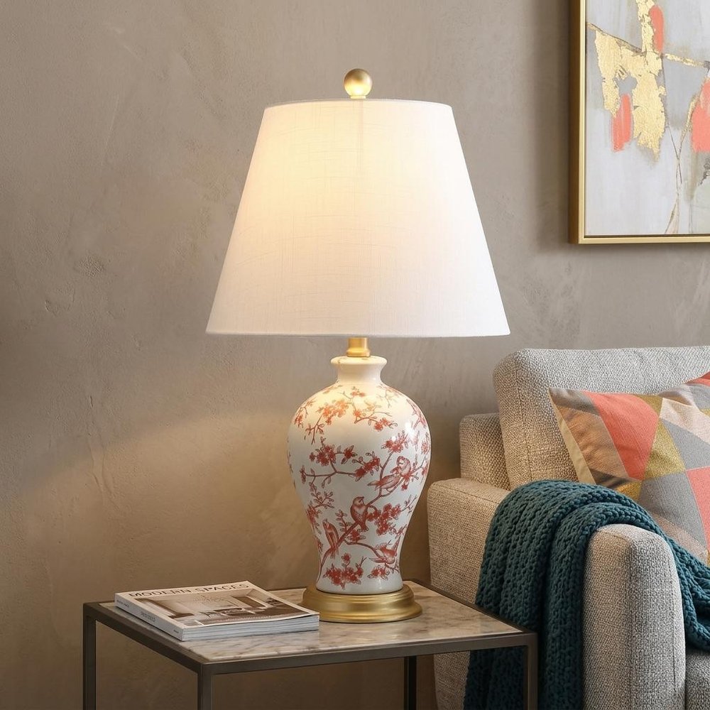 24" Gold Urn Table Lamp With Empire Shade displayed on a dark wood tabletop in a furnished interior against a tan wall.