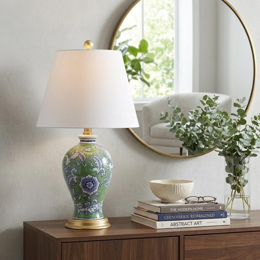 24" Green And Gold Urn Table Lamp With Empire Shade displayed on a dark wood tabletop in a furnished interior against an off-white wall.
