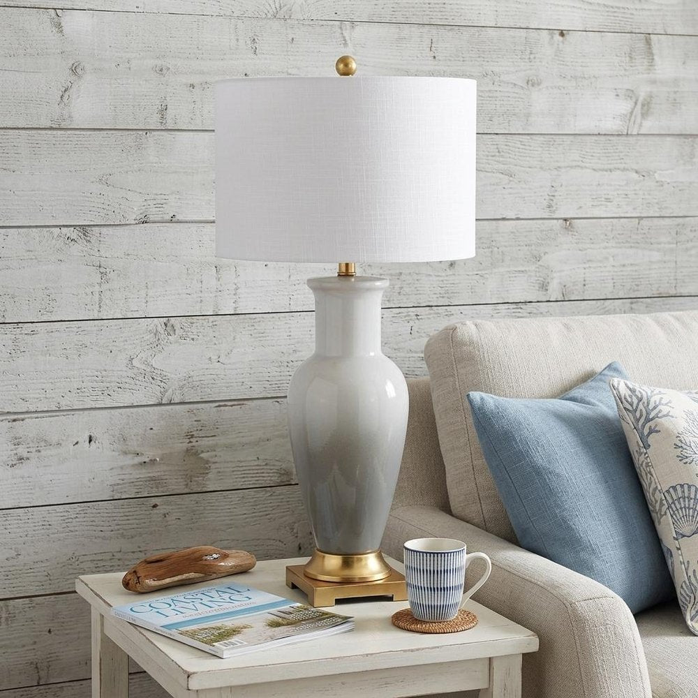 32" Gold Novelty Table Lamp With Drum Shade displayed on a tabletop in a furnished interior against a light gray wall.
