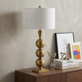33" Gold Novelty Table Lamp With Drum Shade displayed on a dark wood tabletop in a furnished interior against a light gray wall.