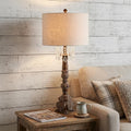 34" Brown Novelty Table Lamp With Drum Shade displayed on a dark wood tabletop in a furnished interior against an off-white wall.