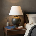 26" Dark Gray Novelty Table Lamp With Drum Shade displayed on a dark wood tabletop in a furnished interior against a dark brown wall in charcoal.