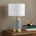 25" Gold Novelty Table Lamp With Globe Shade displayed on a dark wood tabletop in a furnished interior against a tan wall.