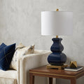 26" Gold Novelty Table Lamp With Globe Shade displayed on a dark wood tabletop in a furnished interior against a light gray wall.