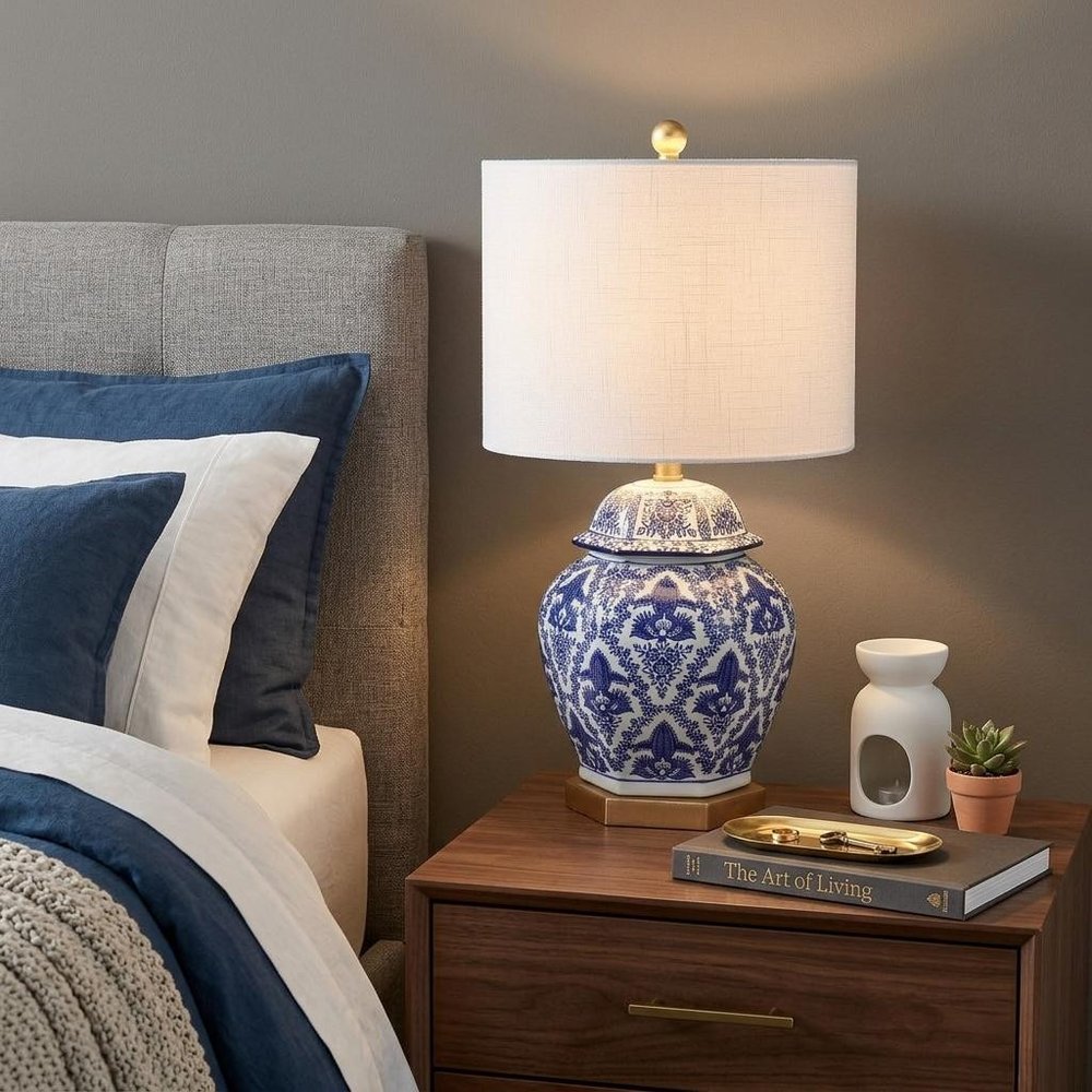 25" Gold Novelty Table Lamp With Drum Shade displayed on a dark wood tabletop in a furnished interior against a gray wall.