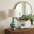 31" Gold Round Table Lamp With Globe Shade displayed on a dark wood tabletop in a furnished interior against an off-white wall.