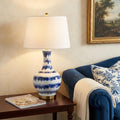 31" Blue White And Gold Novelty Table Lamp With Globe Shade displayed on a tabletop in a furnished interior against a cream wall.